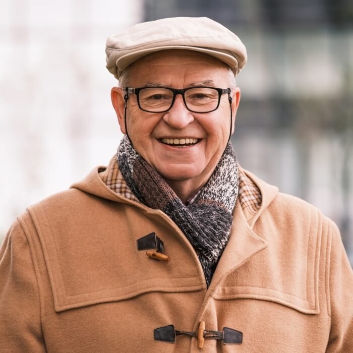 Homme senior souriant portant casquette, lunettes et écharpe en extérieur